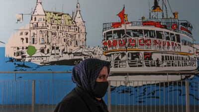 A woman wearing a face mask walks past a city-sponsored graffiti mural depicting the historical Haydarpasa Train Station (left) and the famous ferry (right) at a metrobus station in Istanbul, Turkey. EPA