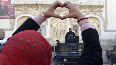 A Tunisian woman makes a heart sign as she stands in front of security forces guarding the area during a rally marking the ninth anniversary of the 2011 uprising on Habib Bourguiba Avenue in central Tunis on January 14, 2020. AFP