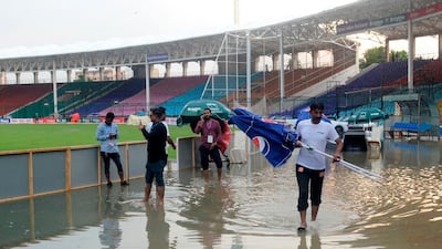 Ground staff members wade in rain water at the National Stadium in Karachi. AFP