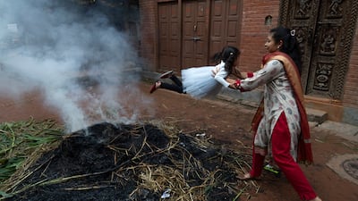 A mother swings her child around smoke where a straw effigy of the mythical demon Ghanta Karna was burnt during celebrations of the Hindu festival Gathemangal in Bhaktapur, Nepal. EPA