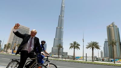 London mayor Boris Johnson salutes photographers as rides a bicycle in front of Burj Khalifa, the world's tallest tower, during his visit to Dubai, on April 16, 2013. AFP PHOTO/KARIM SAHIB (Photo by KARIM SAHIB / AFP)