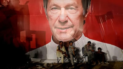 Labourers, who set up the venue, sit under a wall with a billboard displaying a photo of Imran Khan. Reuters