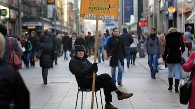 A man holds a sales board promoting the services of an 'Irish Fortune Teller', in the O'Connell Street shopping district as pedestrians walk past retail stores in Dublin, Ireland, on November 25, 2011. Hammered by austerity measures a year after receiving a massive EU-IMF bailout, Ireland is hailed as a eurozone poster boy for the way it is coming to terms with the consequences of its boom to bust. AFP PHOTO / PETER MUHLY *** Local Caption *** 345541-01-08.jpg