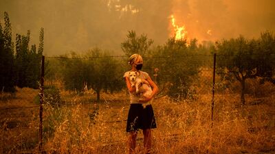A woman cradles a dog as fires approach the village of Pefki, on Evia.