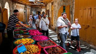 Jewish settlers guarded by Israeli security forces walk past a market stall on the Palestinian side of the old city market in the occupied West Bank city of Hebron. AFP / Hazem Bader