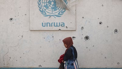 A Palestinian woman walks past a damaged wall bearing the UNRWA logo at a camp for internally displaced people in Rafah in the southern Gaza Strip. AFP