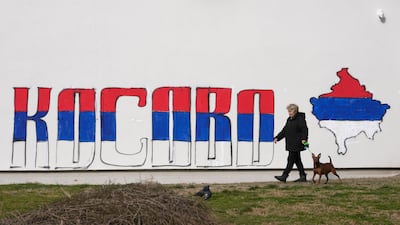 A woman in Belgrade walks past part of a mural depicting maps of Kosovo painted in the colours of the Serbian flag. AP