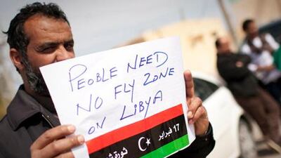 A Libyan man holds up a sign asking for a no-fly zone over Libya near the border town of Musa.
