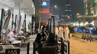 People walk past a coffee shop along Riyadh's commercial Tahlia Street. Business activity and new work were affected by the war in March. AFP
