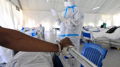 A Kenyan medical staff member checks the medical records of a Covid-19 patient and a prisoner while his hand is handcuffed on his bed in an isolation ward in Machakos, Kenya. EPA
