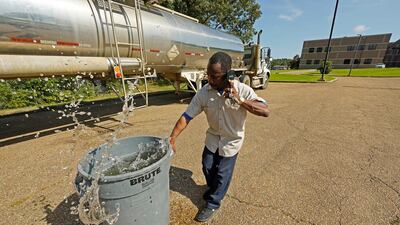Santonia Matthews, a custodian at Forest Hill High School in Jackson, Miss. , hauls away a trash can filled with water from a tanker in the school's parking lot, Wednesday, Aug. 31, 2022. The tanker is one of two placed strategically in the city to provide residents non-potable water. The recent flood worsened Jackson's longstanding water system problems and the state Health Department has had Mississippi's capital city under a boil-water notice since late July. (AP Photo/Rogelio V. Solis)