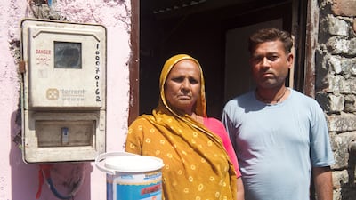 Indiranagar residents stand beside a can of the reflective paint that is being applied on the roof of their home