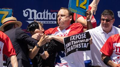 Joey Chestnut tackles a protester who interrupted the competition during the 2022 Nathan's Famous Fourth of July hot dog eating contest on Coney Island on July 4, 2022 in New York. - Joey Chestnut won by eating 63 hot dogs and buns. (Photo by Yuki IWAMURA / AFP)