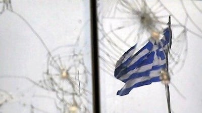 A Greek flag is seen through glass broken during previous protests in Athens. AFP