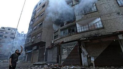 A Free Syrian Army fighter stands in front of a burning building hit by a mortar shell fired by Syrian Army soldiers in the Zamalka neighbourhood of Damascus.
