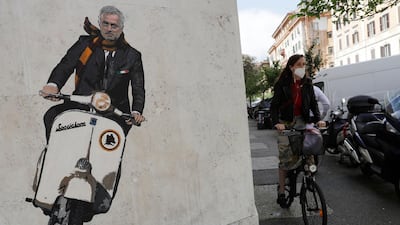 A woman rides her bicycle near a mural depicting Jose Mourinho riding a Vespa scooter adorned with the Roma symbol and wearing a red and yellow scarf in the Testaccio neighbourhood. AP