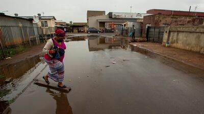 A woman wearing a mask crosses a waterlogged street after rainfall in Thokoza, east of Johannesburg, South Africa. AP Photo