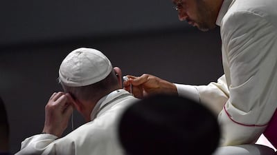 Pope Francis adjusts his earphones. AFP