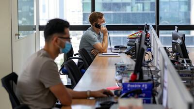 Employees work at their desks with their masks on in Dubai. Chris Whiteoak / The National