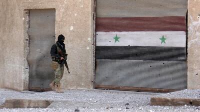 A rebel fighter walks past a shutter bearing the Syrian flag in the village of Rahbet Khattab, Hama province, on March 23, 2017. Omar Haj Kadour / AFP