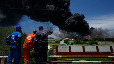 Workers watch a huge plume of smoke rising from the Matanzas depot. The Cuban authorities say lightning struck a crude oil storage tank at the base, causing a fire that led to four explosions. AP