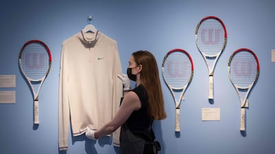 An assistant poses with Swiss tennis champion Roger Federer's cardigan and racket from Wimbledon 2012 (left) and rackets from the Olympics 2012 (right) during a photocall at Christie’s auction house in central London.