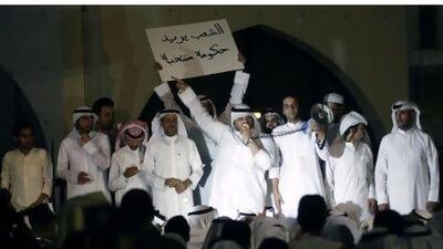 A Kuwaiti protester holds a banner reading "The people want an elected government" as another addresses fellow demonstrators outside the parliament building in Kuwait City late on June 10, 2011 during a rally demanding the resignation of the Gulf state's Prime Minister Sheikh Nasser Mohammed al-Ahmed al-Sabah.