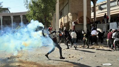 A protester throws back a tear gas canister fired by police during clashes in Baghdad, on Friday. AP Photo