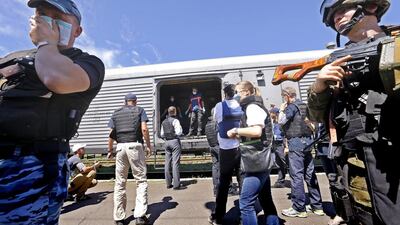 An armed separatist soldier, left, covers his face from the corpses' smell while OSCE inspectors and forensic experts from the Netherlands, background, check the bodybags lying in one of the train's refrigerated coaches that preseves the bodies of the victims of Boeing 777 Malaysia Airlines flight MH17, which crashed during flying over the eastern Ukraine region. Robert Ghement/EPA