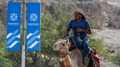 A man rides a camel along a road past signs bearing the name and logo of the conference in Sweimeh. AFP