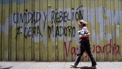 A woman walks past a graffiti reading "Unity and rebellion, out Maduro" in Caracas, on May 2, 2019. AFP