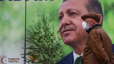 A man wearing a face mask stands in front of a huge poster with a picture of Turkish President Recep Tayyip Erdogan on the facade of a building, in Istanbul, Turkey, 10 May 2023. EPA