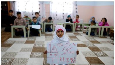 Syrian refugee Islem Halife, 11, as she shows a drawing of her home in Syria, as she sits in a classroom in Nizip refugee camp in Gaziantep province, Turkey. The writing in Arabic in the drawing reads, “God is great.”