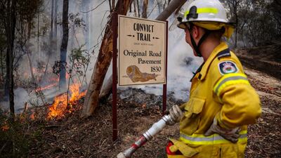 A New South Wales (NSW) Rural Fire Service volunteer watches a fire next to a sign, indicating the site of a convict-built road, during back-burning operations in bushland near the town of Kulnura, New South Wales, Australia. Bloomberg
