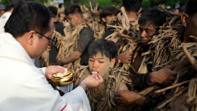 A Catholic boy receives holy communion from a priest during the mud festival at Bibiclat
