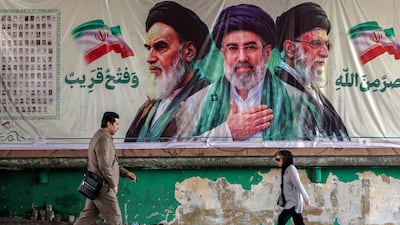 People walk past a banner depicting the portraits of Iran's former supreme leader Ayatollah Ruhollah Khomeini (L), Iran's supreme leader Ayatollah Mojtaba Khamenei (C), and slain supreme leader (Ayatollah Ali Khamenei (R) in Tehran on October 21, 2026. (Photo by ATTA KENARE / AFP)