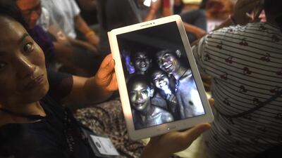 A happy family member shows the latest pictures of the missing boys taken by rescue divers inside Tham Luang cave. Twelve boys and their football coach trapped for nine days have been found safe. Lillian Sunwanrumpha / AFP Photo