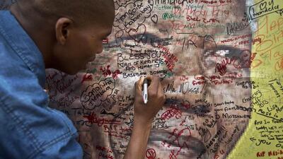 A woman writes a message on a poster of Nelson Mandela outside his old house in Soweto, South Africa. Tributes to Mandela flooded in from across the world after his death was announced on Thursday. Ben Curtis / AP Photo