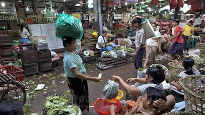 A retail seller, balancing a bag of betel leaves on her head, pays for what she bought from a wholesale vender at a market in suburban Yangon, Myanmar. Gemunu Amarasinghe / AP