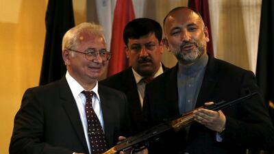 Russian ambassador to Afghanistan Alexander Mantytskiy, left, giving an AK-47 to recently resigned Afghan national security adviser Hanif Atmar in 2016. Mr Atmar cited 'serious differences' in policy on security and national unity in his resignation letter on Saturday. Mohammad Ismail / Reuters