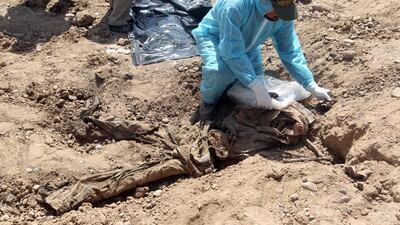 A member of the Iraqi security forces in 2015 wearing protective clothes inspects a mass grave containing the remains of dozens of people believed to have been slain by ISIS. AFP