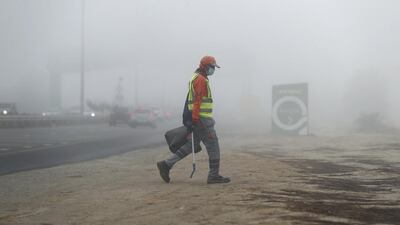 A worker collects rubbish on the side of the road in the fog. Chris Whiteoak / The National