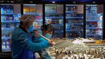 Workers wearing face masks pour ice on the clams at a section selling imported seafoods at a supermarket in Beijing. AP Photo