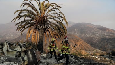 Firefighters Jason Toole, right, and Brent McGill walk among the ashes of a wildfire-ravaged home in Malibu. AP Photo