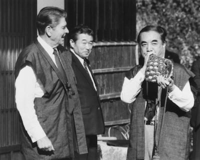 Yasuhiro Nakasone blows a conch shell next to US President Ronald Reagan during their summit meeting in Hinode Town, Tokyo on November 11, 1983. Kyodo via Reuters