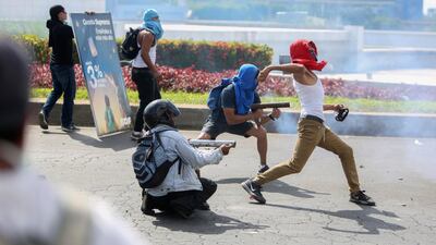 Masked protesters fire homemade mortars at riot police as another protester throws a rock during a third day of violent clashes in Managua, Nicaragua. Alfredo Zuniga / AP Photo