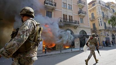 Lebanese soldiers clear the road next to a burning bank branch, set ablaze by demonstrators following the funeral of protester Fawaz al-Samman, in the northern port city of Tripoli. AFP