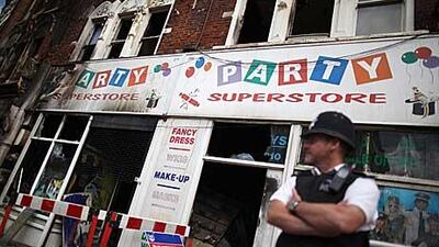 A policeman stands outside a fire-damaged shop in Clapham Junction, London, yesterday. As trouble erupted through the night in other major cities across England, London remained mostly quiet after 16,000 police were deployed.