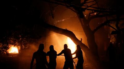 People try to extinguish a burning house during a wildfire in the Nea Kifisia suburb north of Athens.
