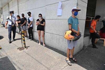 A private security guard, left, inspects customers queueing up as they practise social distancing outside a bank in Manila. AFP